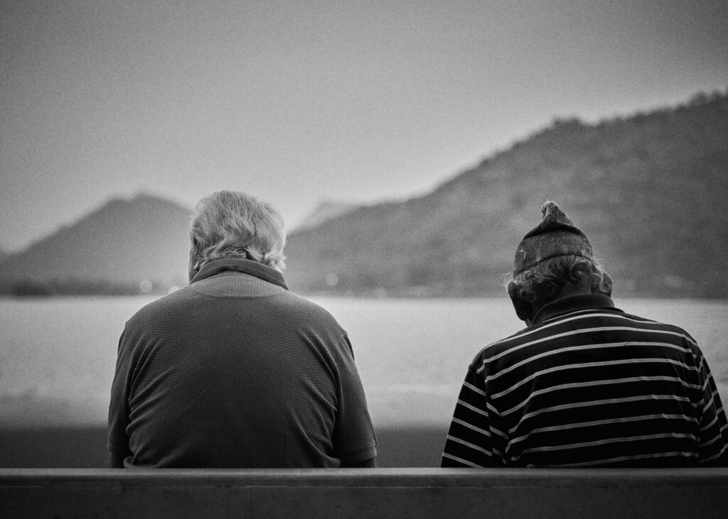 Two elderly People sitting on a bench looking at river