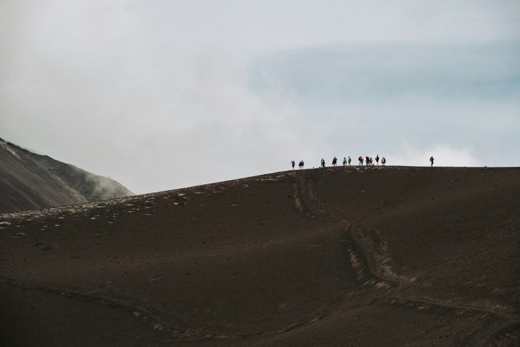 Travelers standing atop a volcanic crater at sunrise, overlooking Vulcano Hotel Garden dramatic landscape.