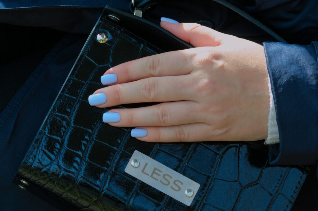 French tip nail designs on neatly manicured hands resting on a black bag.