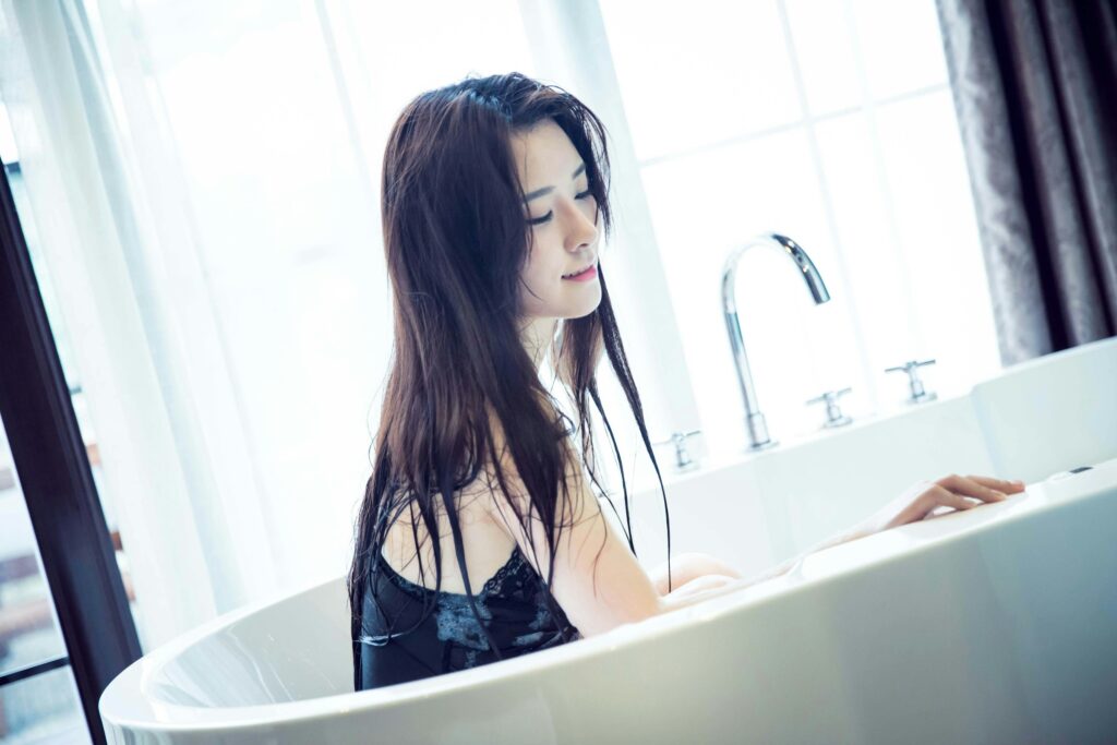 Woman relaxing in a bubble bath with wet hair, enjoying a fresh wash with the best clarifying shampoo for curls, color, and volume.