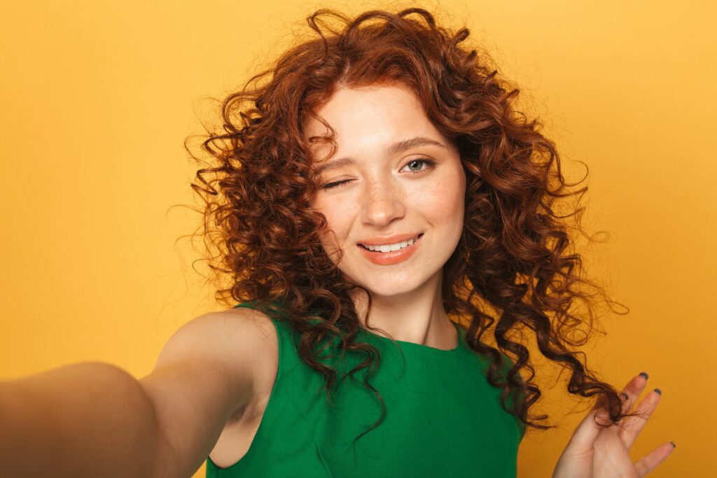 Woman with red Irish curls wearing a green dress, showcasing natural curly hairstyle.