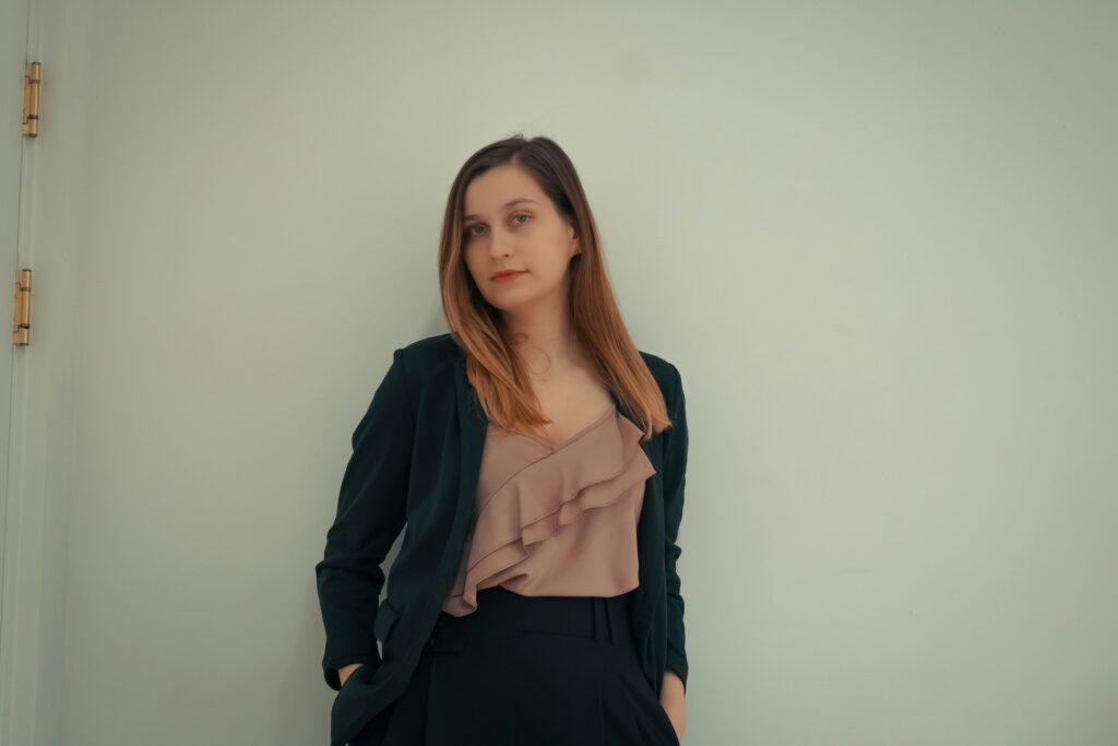 Confident woman in professional outfit standing against a white wall, embodying office siren aesthetic.