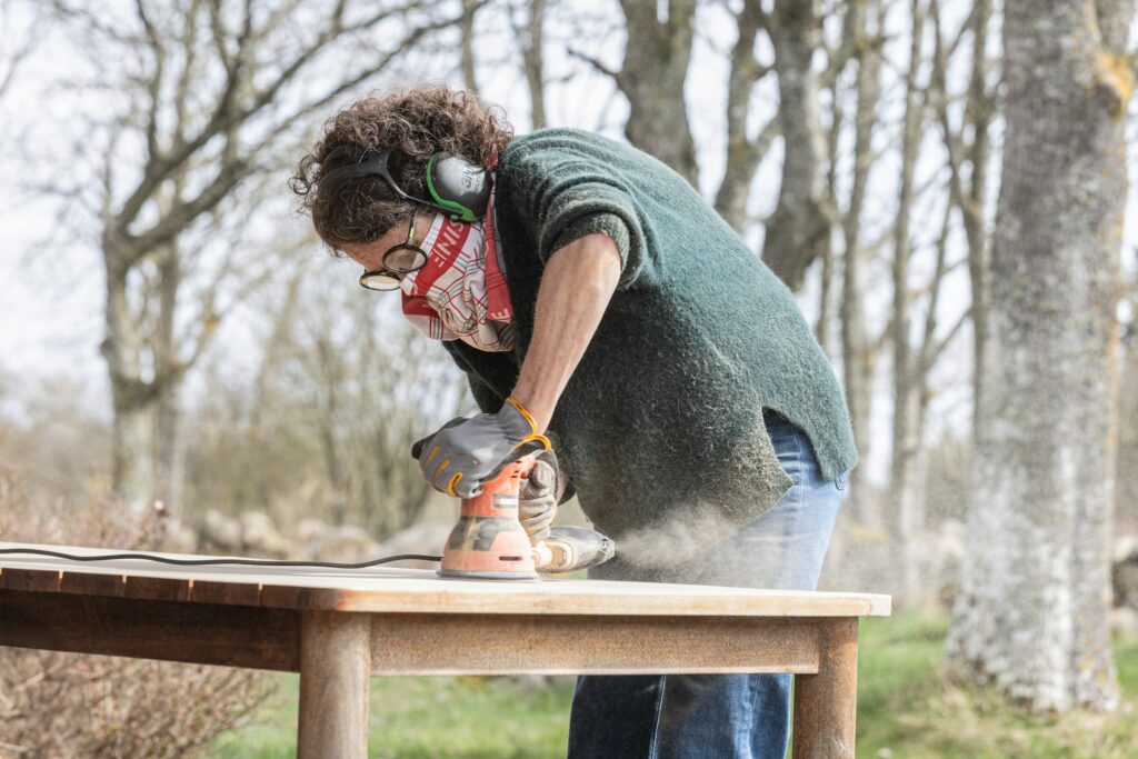 Using the best sander for furniture restoration, a woman sands a wooden table outdoors.