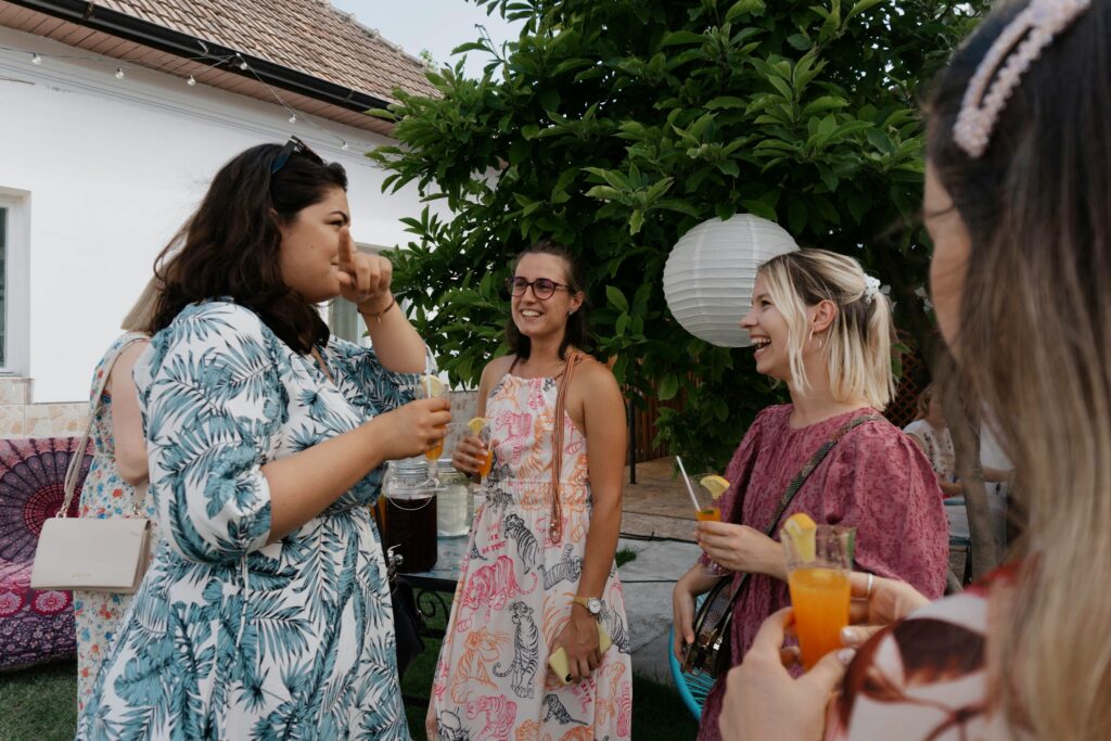 Women wearing elegant tea party outfits in soft florals and pastels, standing together at an outdoor gathering.