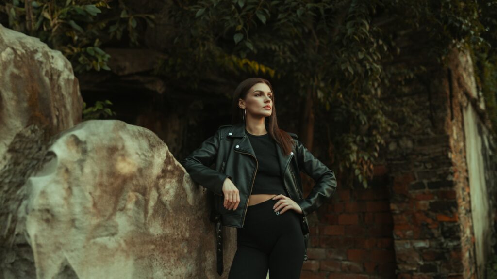 Woman wearing a sleek black jumpsuit leaning against a stone wall, styled for a modern and versatile fashion look.