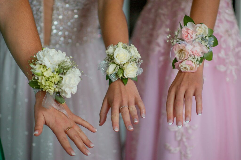 Three women wearing corsage on their wrists, highlighting stylish wrist corsage ideas for formal events like prom and weddings.