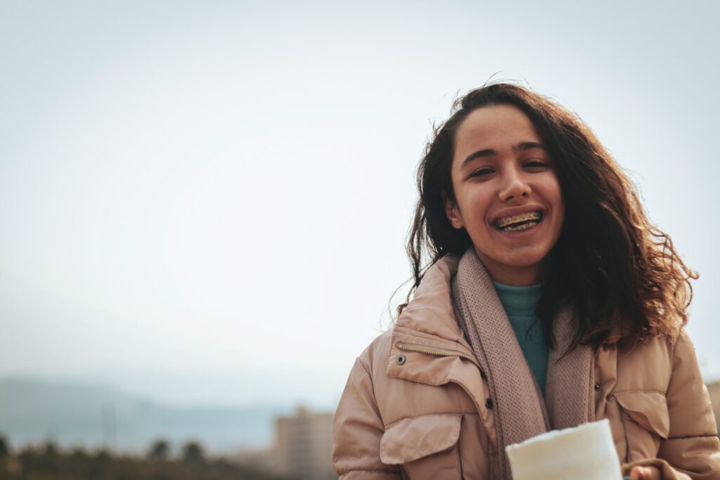 Woman smiling confidently with a permanent retainer while holding a cup of coffee.