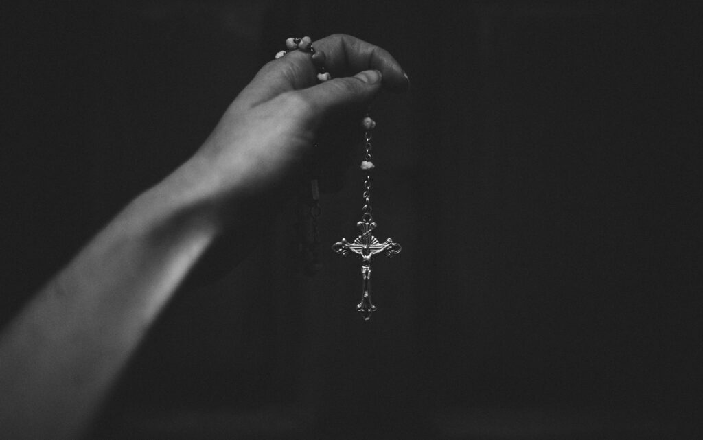 Grayscale image of person holding a rosary necklace, showcasing spiritual and fashion elements