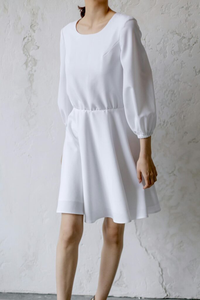 Woman wearing an elegant white drop waist dress standing against a textured wall.