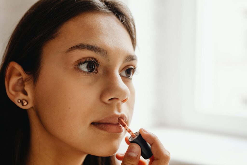 Close-up of a woman applying lipstick as a lip plumper for a naturally full pout.