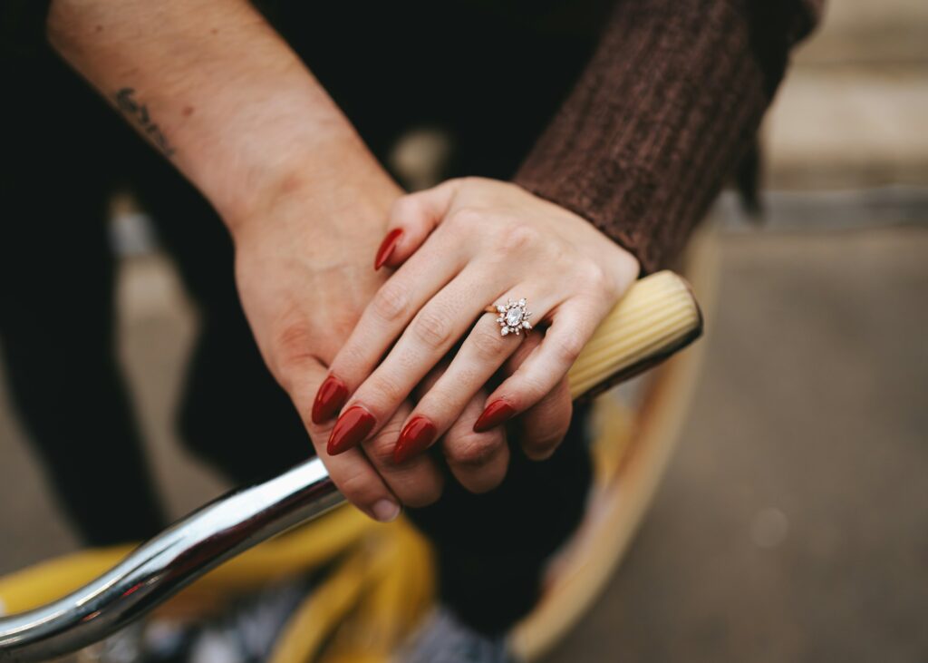 A woman’s hand wearing an oval shape ring resting on a man’s hand, showcasing the beauty of oval engagement rings.
