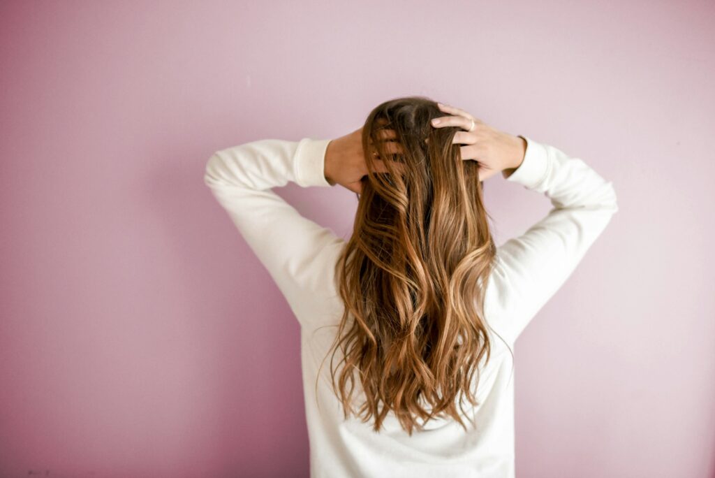 Woman with straight, shiny hair standing against a pink wall, showcasing a smooth silk press hairstyle.