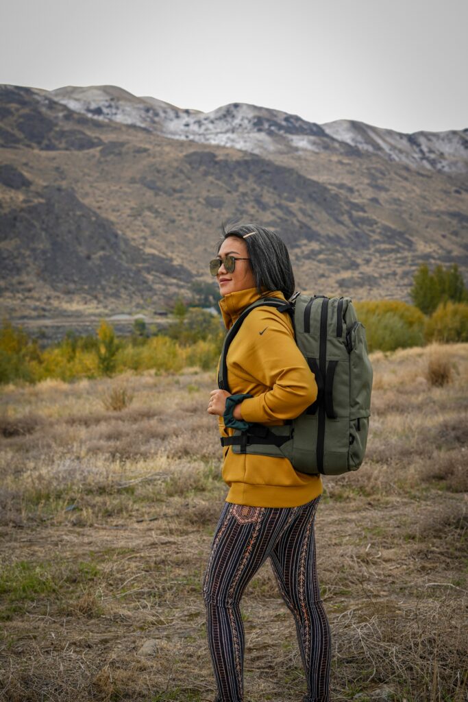 Best travel backpack for women in green tone, worn with casual top and leggings while standing in a grassy outdoor field.