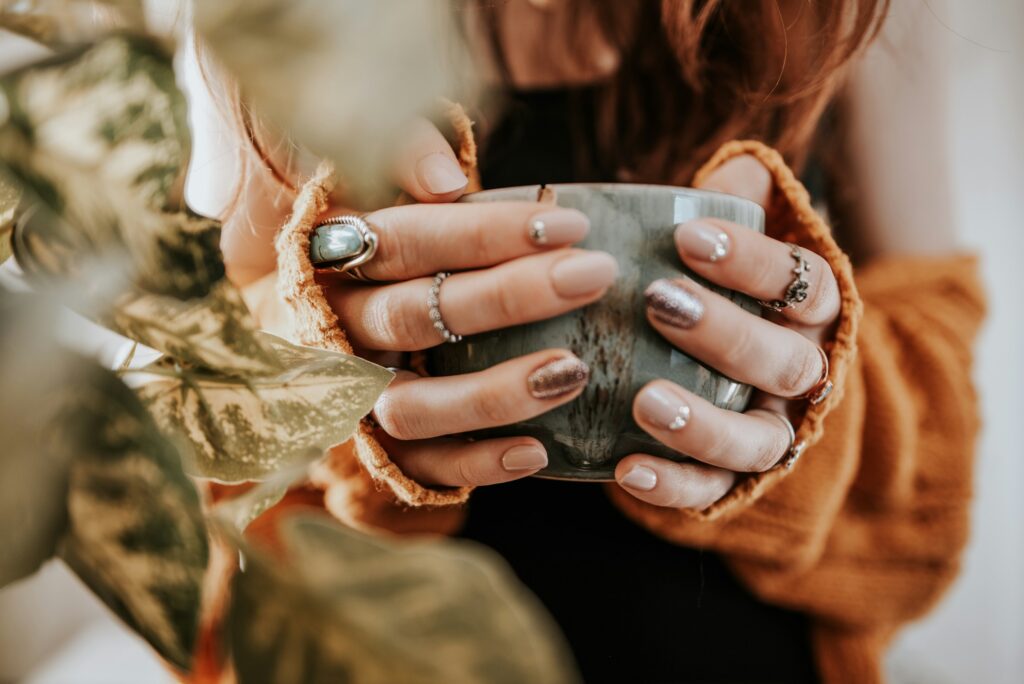 Close-up of trendy chrome nail designs on manicured hands holding a cup.