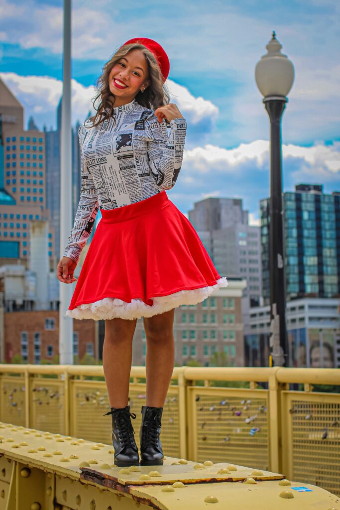 Woman wearing a red bubble skirt styled with a newspaper print top and beret, showcasing a chic street style look in the city.
