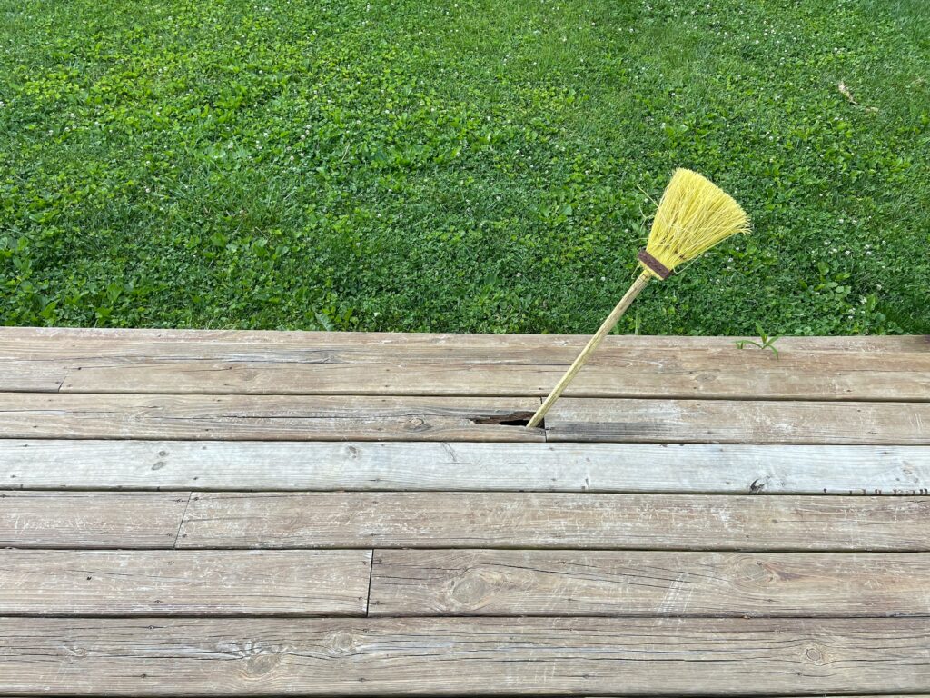 Old wooden deck with a broom stuck between boards, showing wear before deck cleaning.