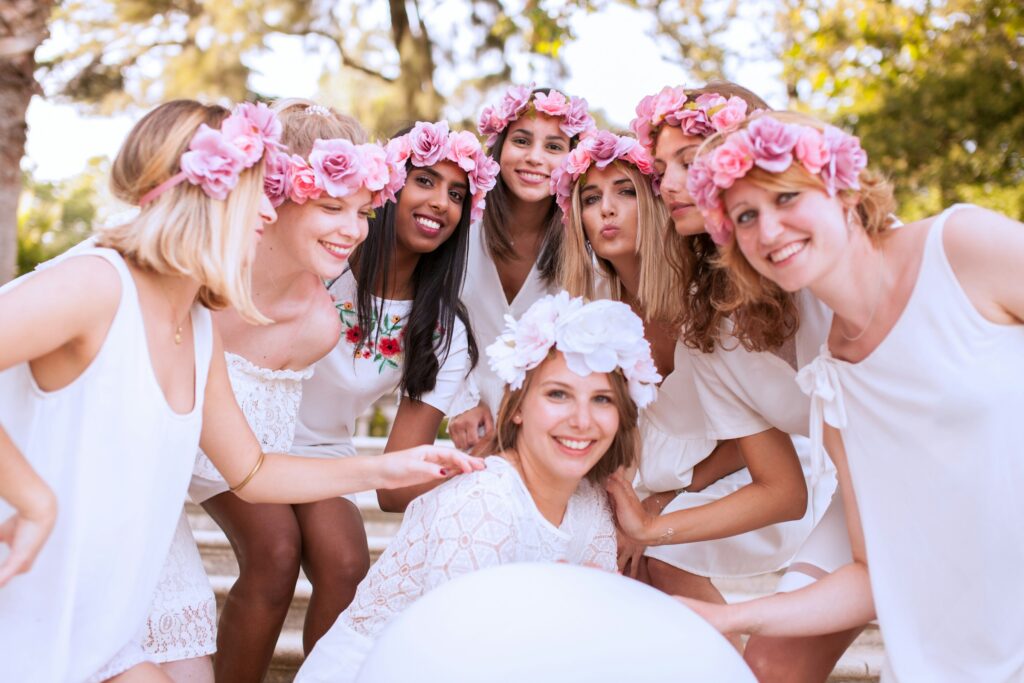 Group of women in white dresses with floral crowns celebrating together at a white party outdoors.