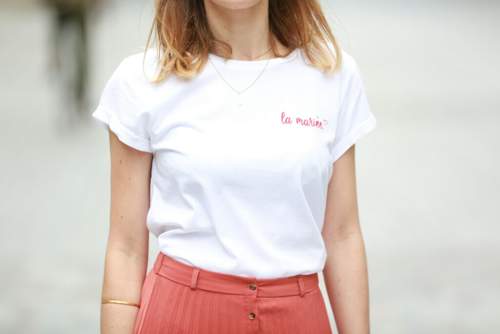Woman styling a white ringer tee with “la mariée” text, tucked into coral high-waisted pants for a chic streetwear look.