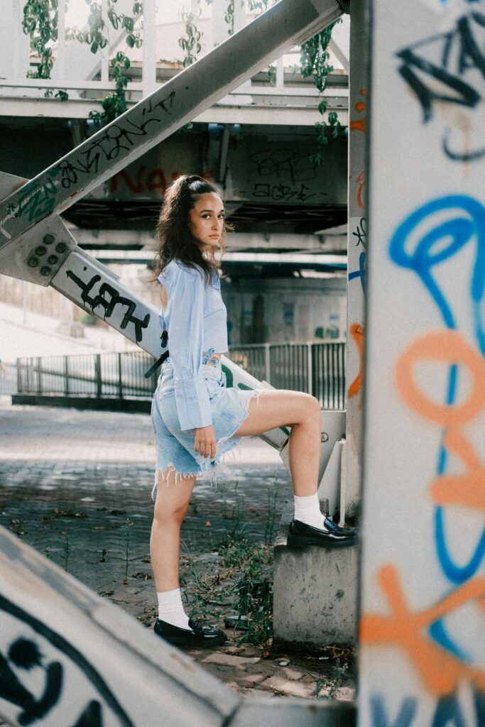 Woman wearing platform loafers styled with white socks, denim skirt, and blue blouse in an urban street setting.