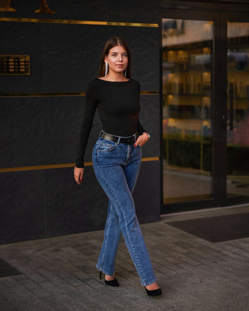 Confident model in low rise baggy blue jeans, black bodysuit, belt, and heels outside modern building – 2026 denim trend.