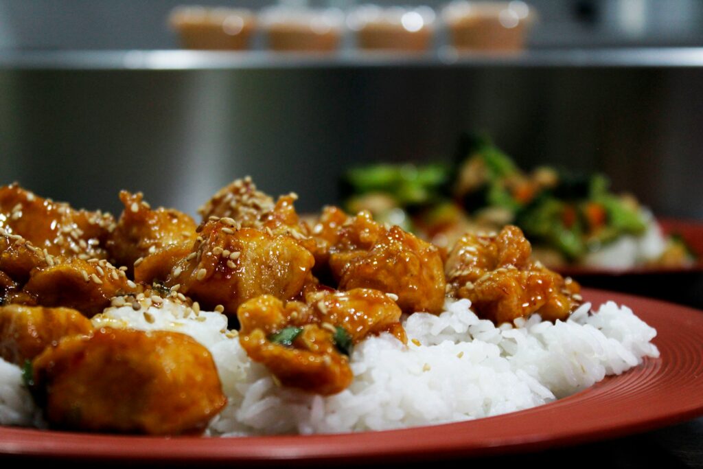 Close-up of chicken teriyaki bowl with glossy sesame sauce, tender chicken pieces on white rice, garnished with green onions.