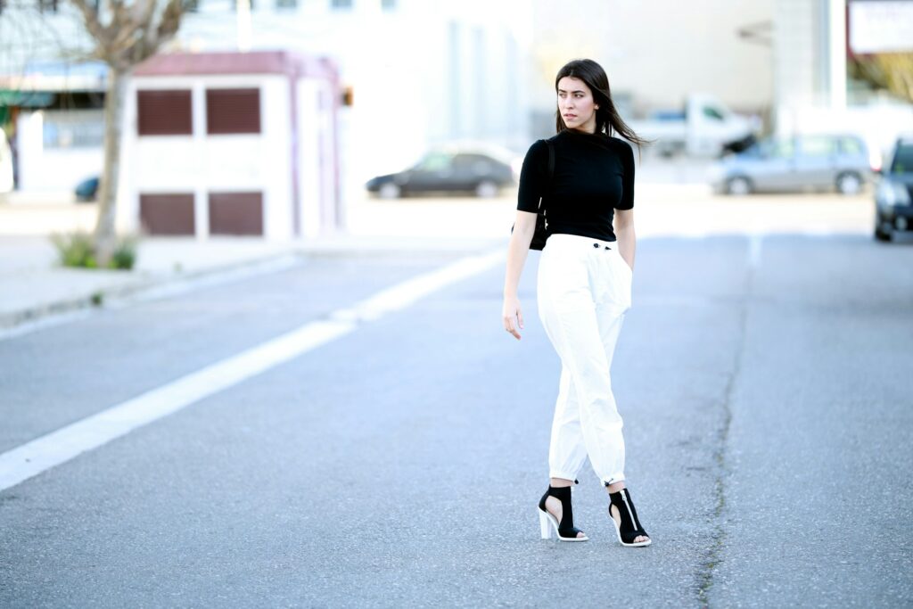 Woman wearing white jeans with black top and heels walking on street, chic modern outfit.