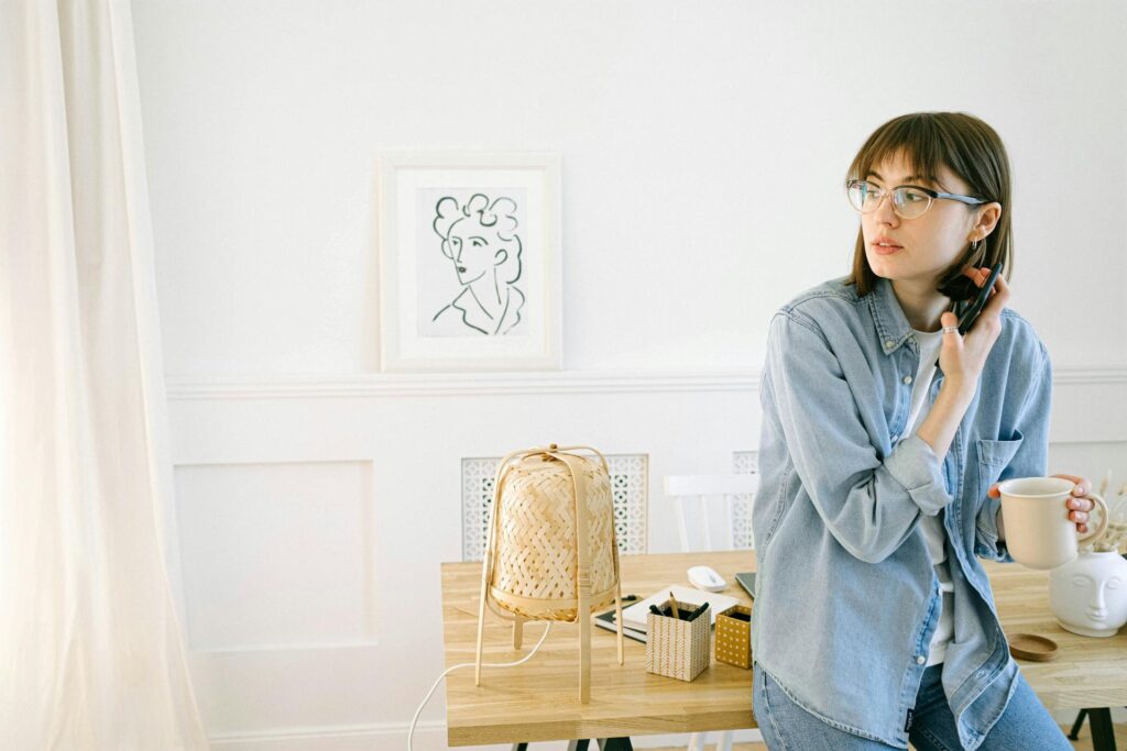 Woman wearing a light blue chambray shirt while sitting in a bright minimalist home office with a coffee mug.