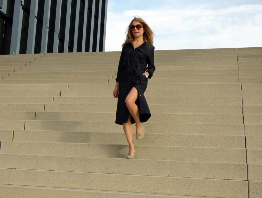 Woman in black shirt dress and nude pumps walking down outdoor stairs — black dress footwear styling guide 2026