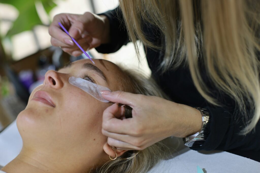 Brow lamination treatment being applied by technician on a client at a beauty salon.