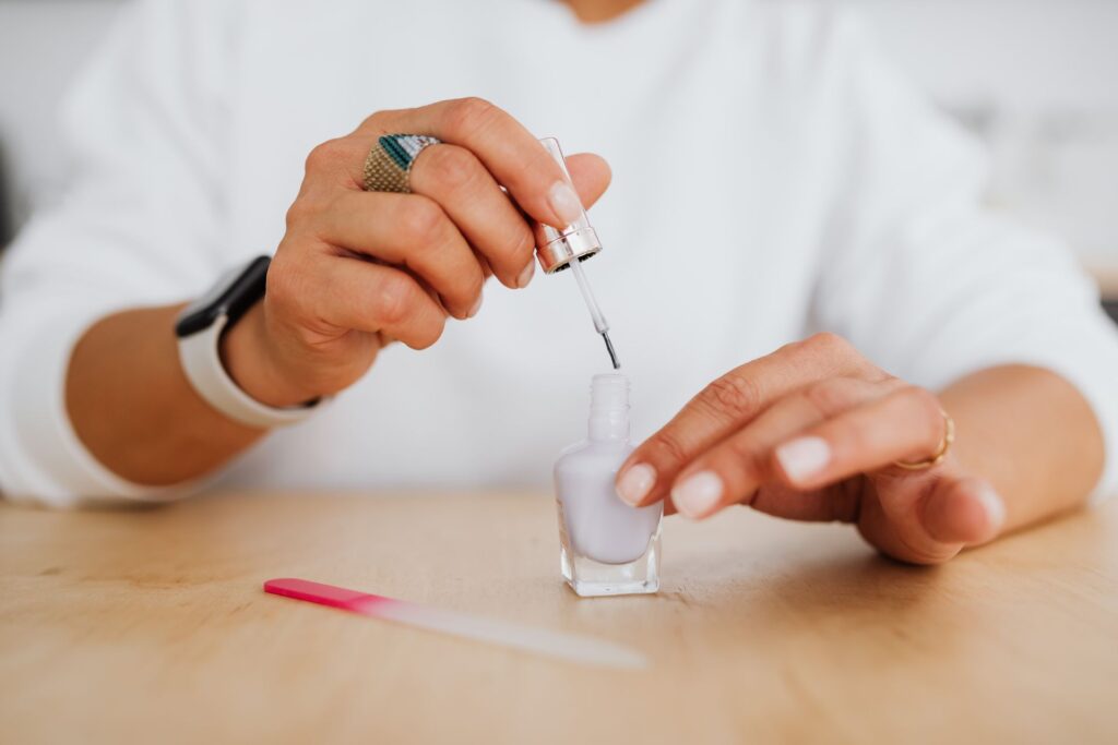 Woman opening a nail glue bottle at home with a nail file on a wooden table.