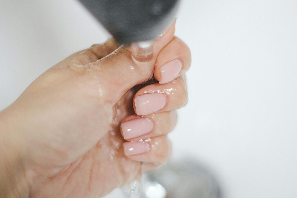 Woman with soft pink soap nails with wet glossy finish under running water.