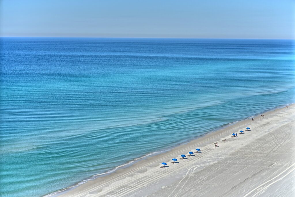 Aerial view of a quiet Gulf Coast beach in Florida with a row of blue umbrellas along the shoreline. 