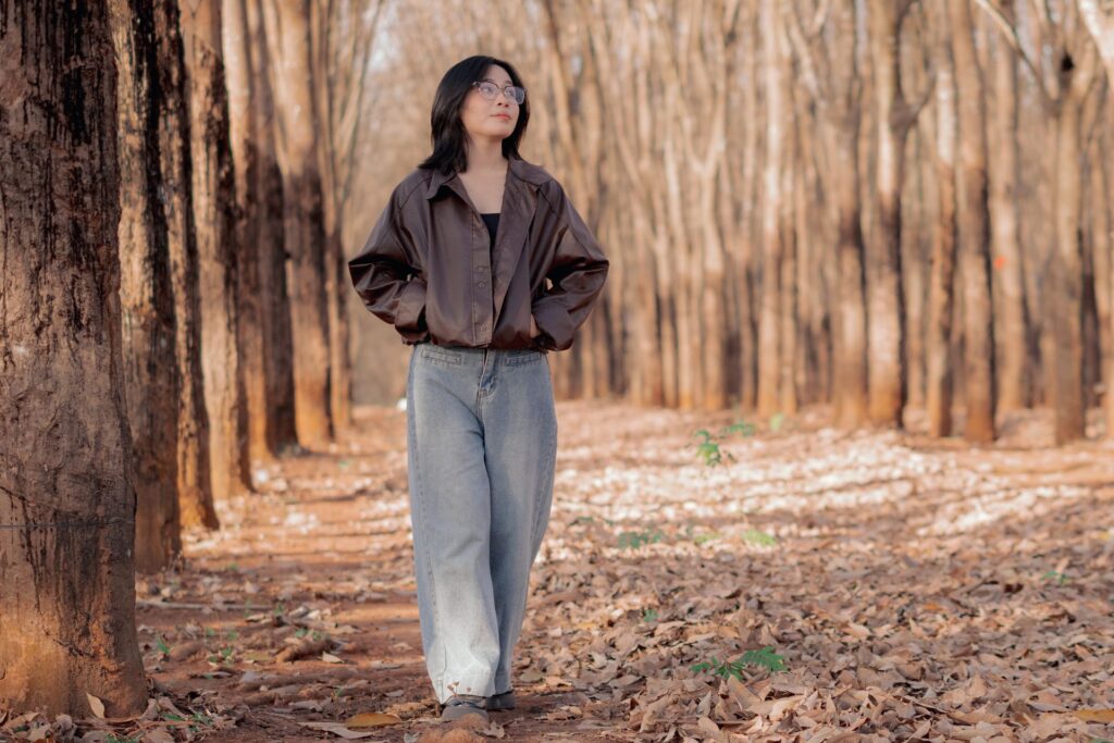 Woman wearing light-wash barrel jeans with a cropped brown leather jacket, showing the waist-defined, tapered silhouette.