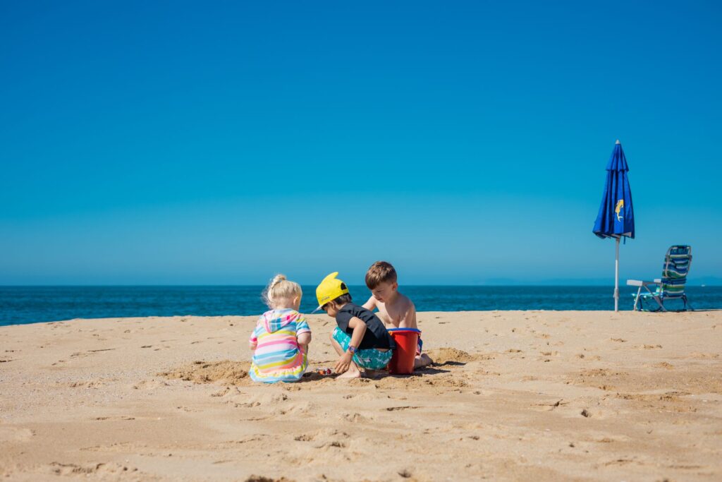 Three young children playing in the sand near a beach umbrella and chair on a family-friendly Florida beach,.