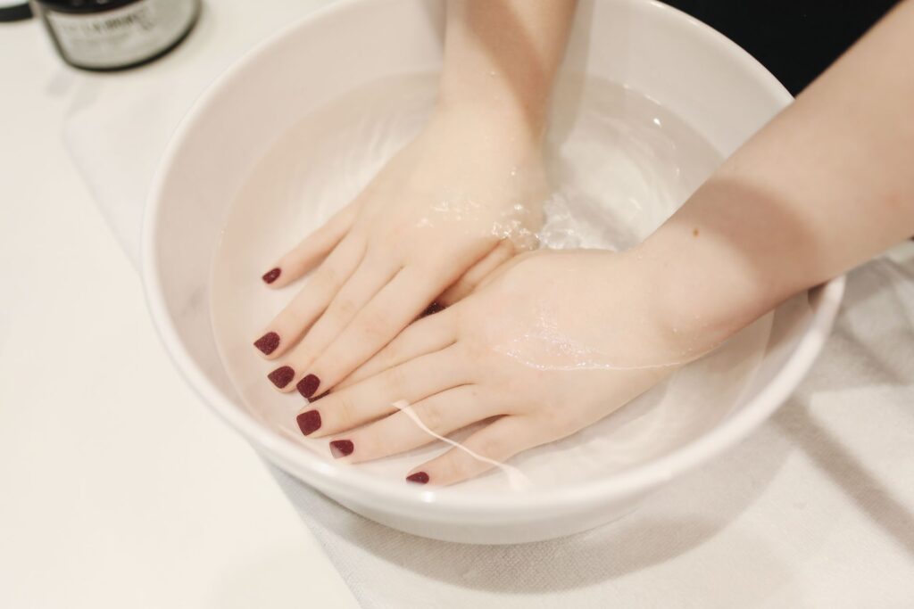 Woman soaking gel-polished nails in warm water at home during the gel nail polish removal process.