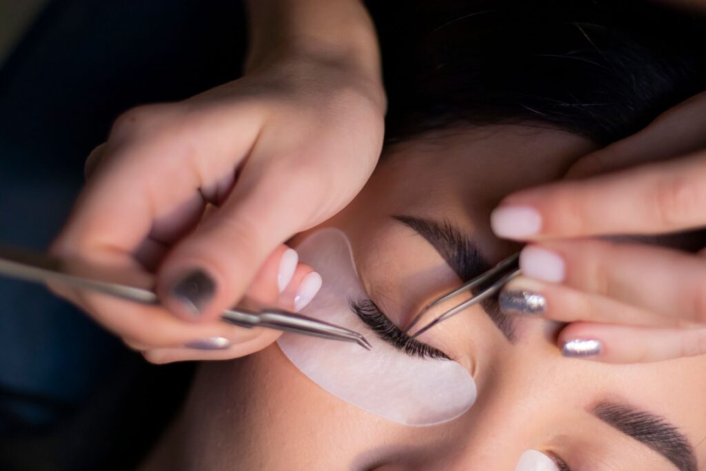 Close-up of a lash lift treatment, with a technician using tweezers to lift natural lashes over a silicone shield.
