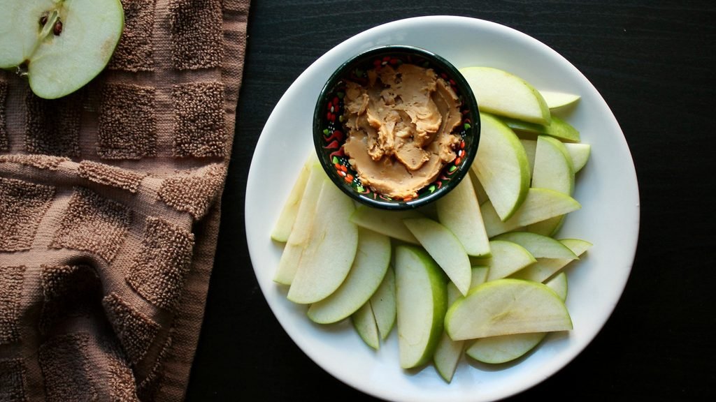 Sliced green apple with a bowl of peanut butter, a zero-prep high protein snack