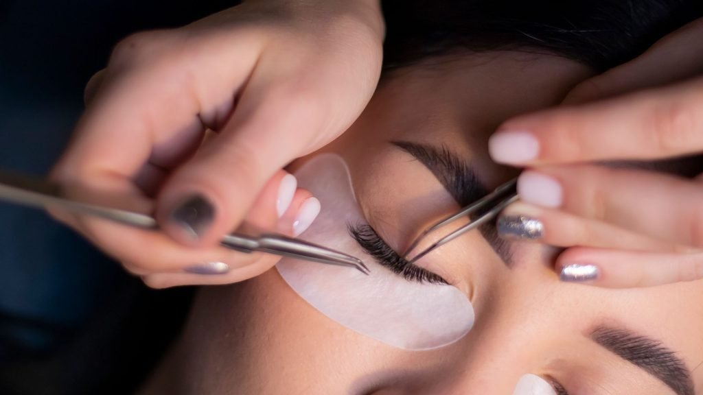 Lash technician applying hybrid lash extensions with tweezers.