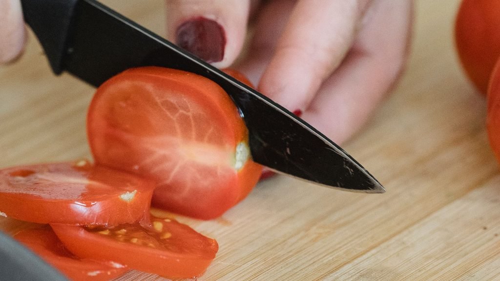 Ripe tomato being sliced into rounds on a wooden board, ready to plant.