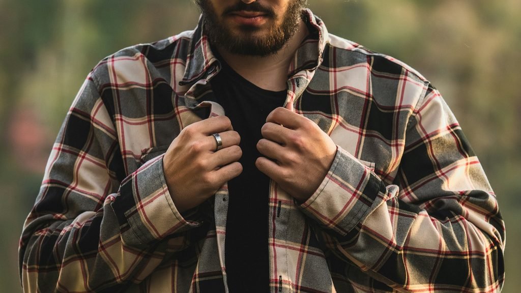 Man wearing plaid shirt clothing in black, white and red, open over a black t-shirt.